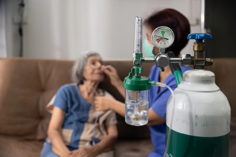 In-Home Oxygen Therapy Administration Elderly woman receiving oxygen therapy with a nasal cannula at home, assisted by a healthcare worker.