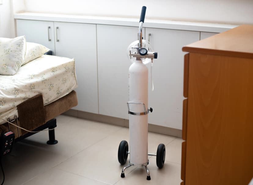 Home Oxygen Therapy Setup A portable oxygen cylinder with a regulator and wheels positioned beside a bed in a home setting.